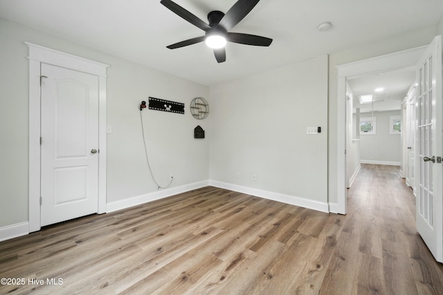 empty room with baseboards, attic access, wood finished floors, and a ceiling fan