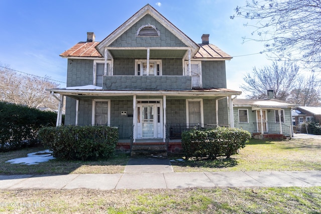 view of front facade with a front yard, a balcony, a porch, and a chimney