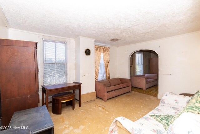 living room featuring visible vents, arched walkways, a textured ceiling, and ornamental molding