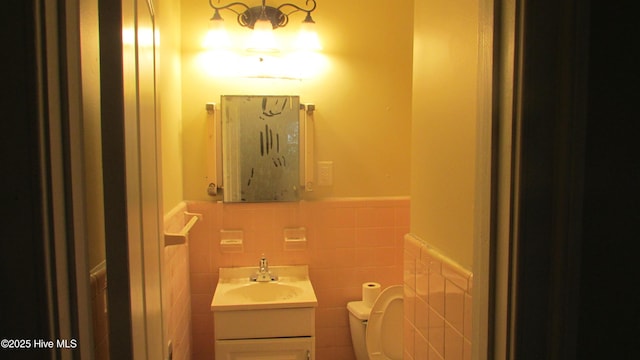 bathroom featuring tile walls, wainscoting, toilet, and vanity