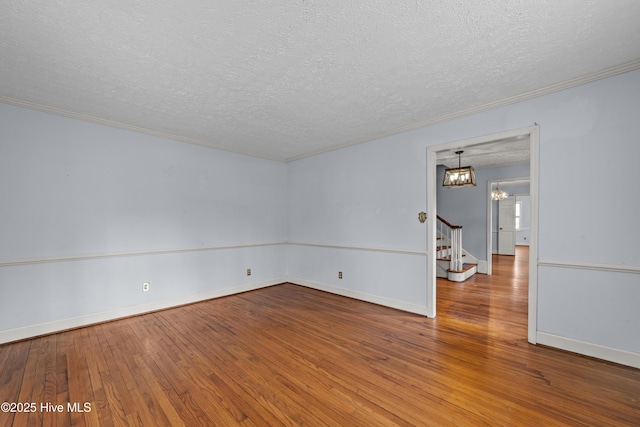 spare room featuring hardwood / wood-style floors, stairway, a notable chandelier, and ornamental molding