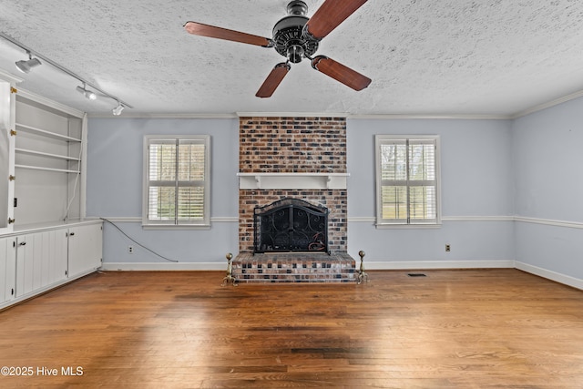 unfurnished living room with a textured ceiling, a healthy amount of sunlight, wood finished floors, and crown molding