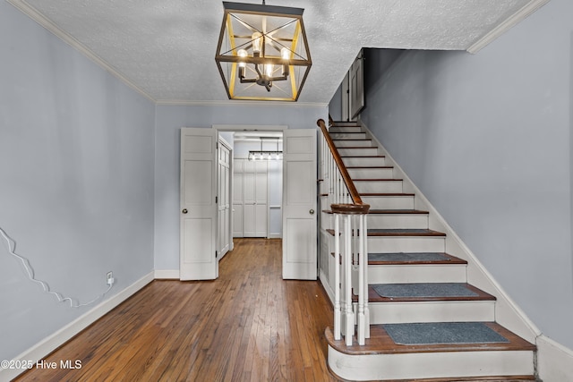 stairway with wood-type flooring, a notable chandelier, crown molding, and a textured ceiling