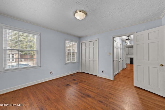 unfurnished bedroom featuring multiple windows, a textured ceiling, crown molding, and wood finished floors