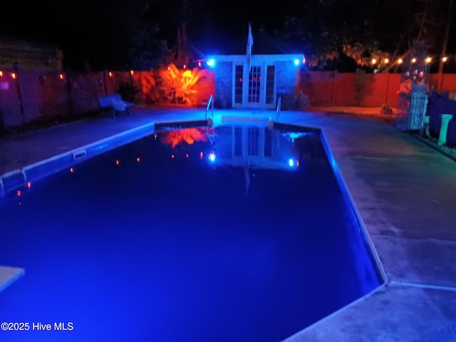 pool at night with an outbuilding, an exterior structure, a fenced in pool, fence private yard, and a patio area