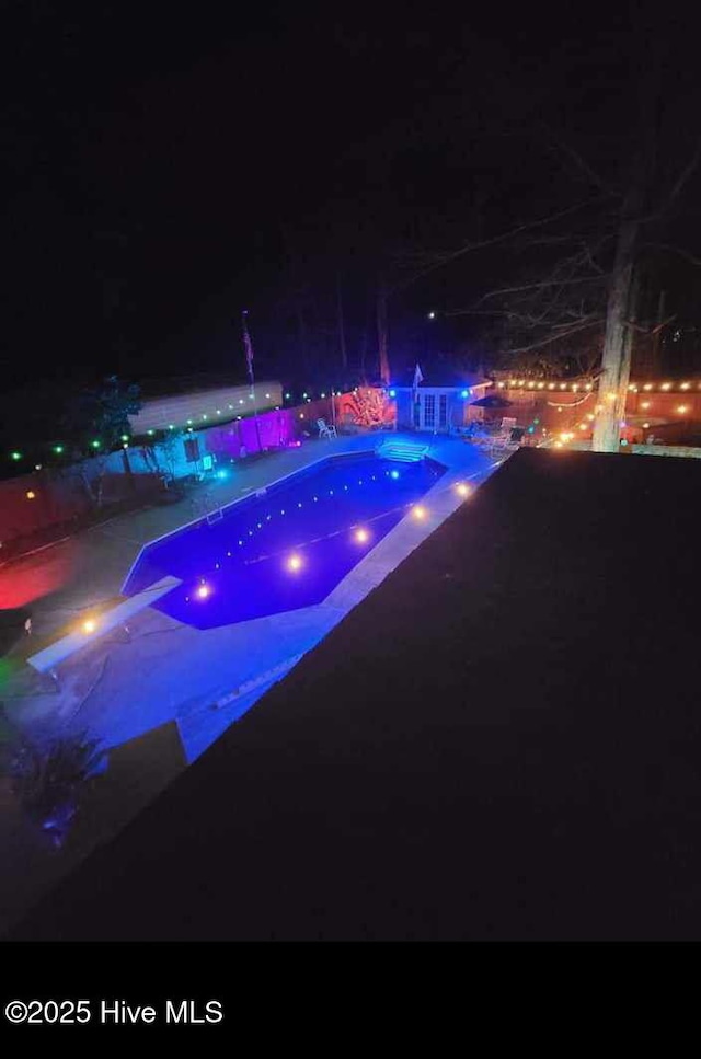 pool at night with an infinity pool, a patio, and a hot tub