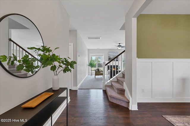entrance foyer featuring a wainscoted wall, visible vents, ceiling fan, stairs, and dark wood-type flooring