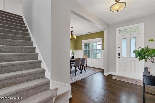 foyer featuring stairs, baseboards, dark wood-style flooring, and a chandelier