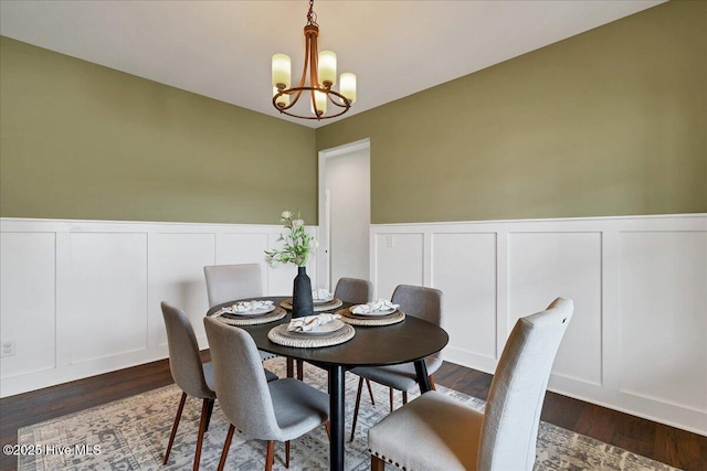dining room featuring an inviting chandelier, a wainscoted wall, and dark wood-style flooring