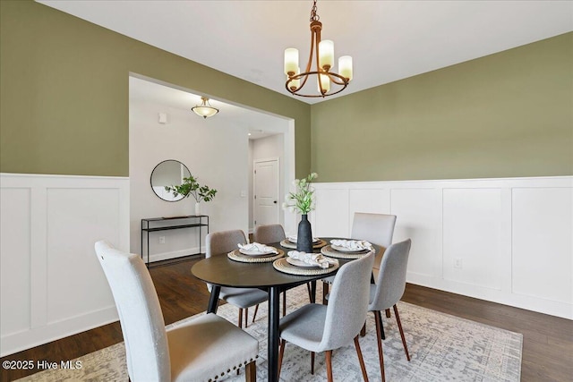 dining space with a decorative wall, wood finished floors, wainscoting, and a chandelier