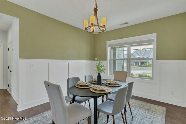 dining area featuring visible vents, a notable chandelier, a wainscoted wall, and dark wood finished floors