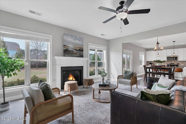 living room with a wealth of natural light, visible vents, and ceiling fan with notable chandelier