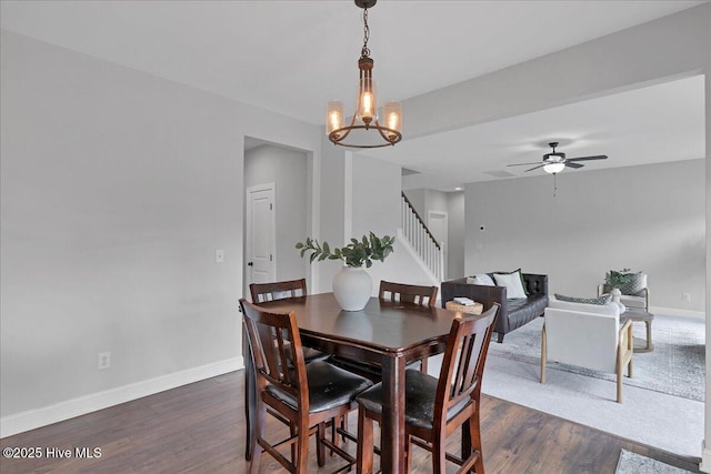 dining room featuring ceiling fan with notable chandelier, stairs, baseboards, and dark wood-style flooring