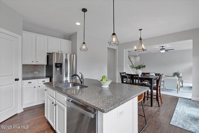 kitchen featuring a sink, a center island with sink, white cabinets, stainless steel appliances, and dark wood-style flooring