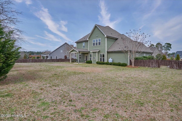rear view of house featuring a shingled roof, a yard, and fence