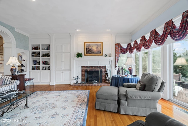 living area featuring ornamental molding, built in features, wood finished floors, arched walkways, and a fireplace