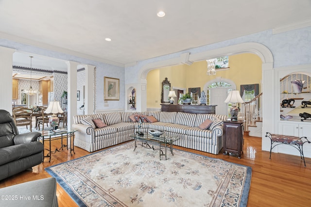 living room featuring wallpapered walls, a chandelier, stairway, ornamental molding, and wood finished floors