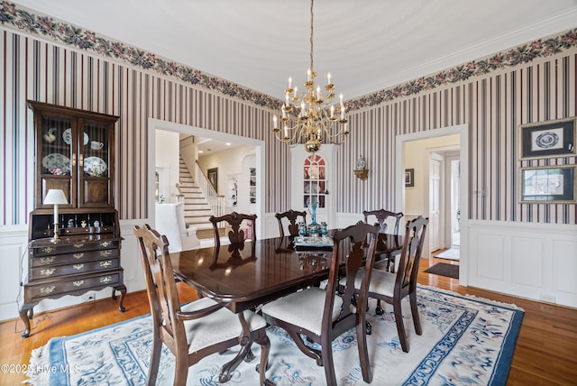 dining room featuring a wainscoted wall, stairway, wood finished floors, and wallpapered walls