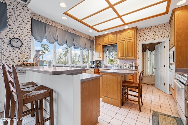 kitchen featuring a breakfast bar area, light tile patterned floors, wallpapered walls, electric stove, and dishwasher