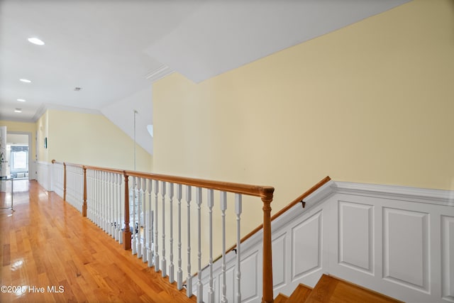 stairway featuring lofted ceiling, wood finished floors, and wainscoting