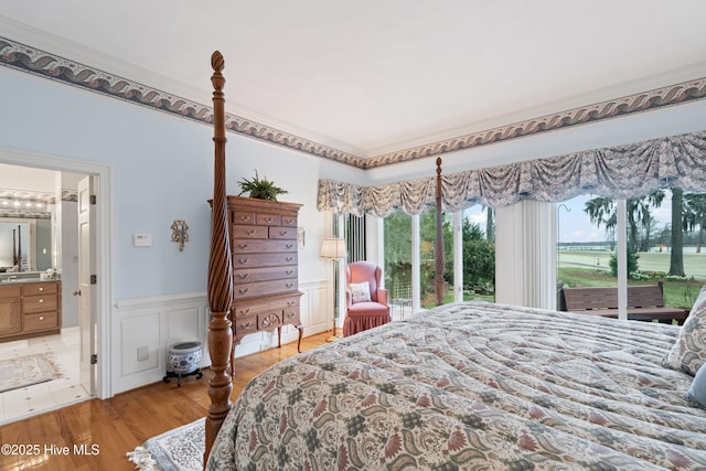 bedroom featuring a decorative wall, multiple windows, a wainscoted wall, and light wood finished floors
