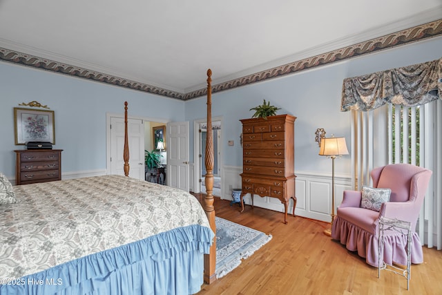 bedroom with light wood-style floors, ornamental molding, wainscoting, and a decorative wall