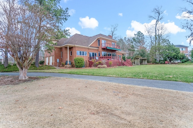 view of front of home featuring a balcony, driveway, a chimney, a front lawn, and brick siding