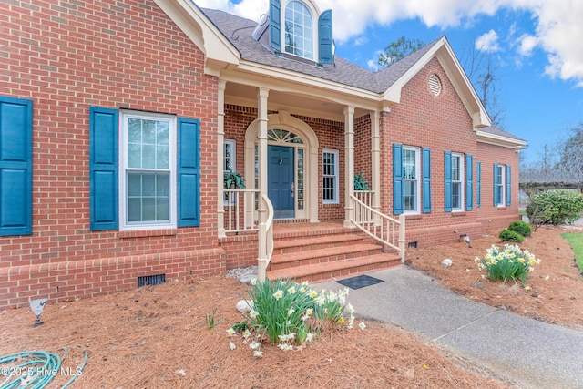 view of exterior entry featuring crawl space, brick siding, and roof with shingles