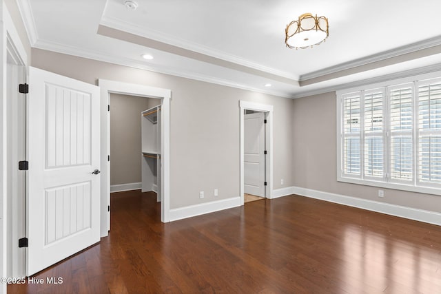 unfurnished bedroom featuring a walk in closet, crown molding, baseboards, wood finished floors, and a raised ceiling