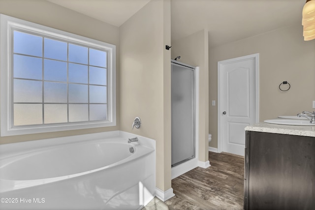 bathroom with baseboards, a shower stall, a garden tub, and wood finished floors