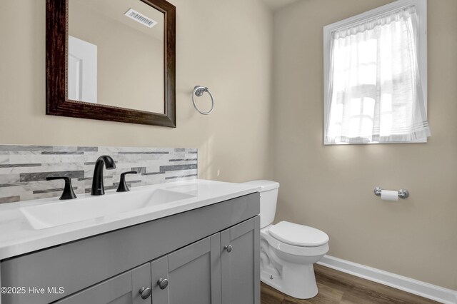 half bathroom featuring visible vents, wood finished floors, toilet, baseboards, and tasteful backsplash