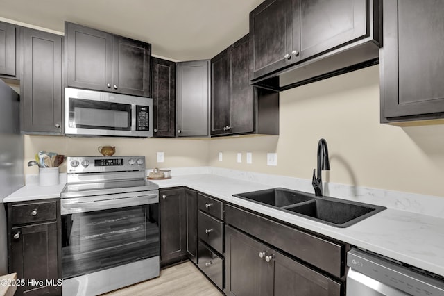 kitchen with light countertops, appliances with stainless steel finishes, a sink, and light wood-style floors