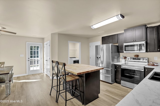 kitchen featuring a breakfast bar area, washer / clothes dryer, appliances with stainless steel finishes, butcher block counters, and light wood-style floors