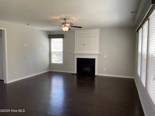 unfurnished living room with baseboards, a fireplace with raised hearth, a ceiling fan, and dark wood-style floors