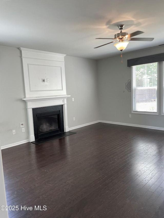unfurnished living room featuring a glass covered fireplace, baseboards, a ceiling fan, and dark wood-style flooring
