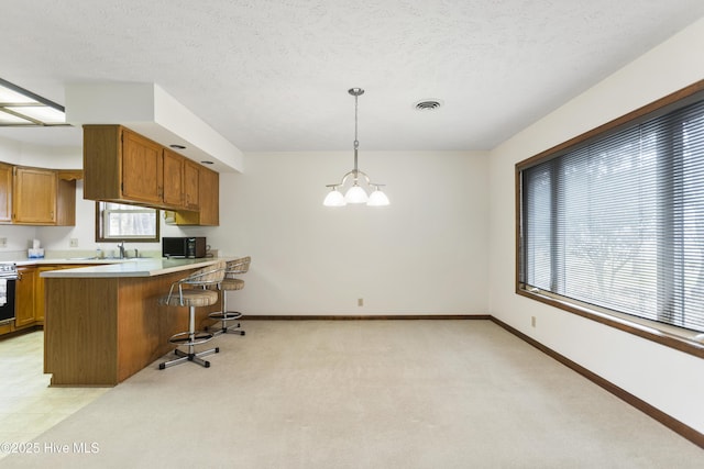 kitchen with brown cabinetry, visible vents, baseboards, light countertops, and a notable chandelier
