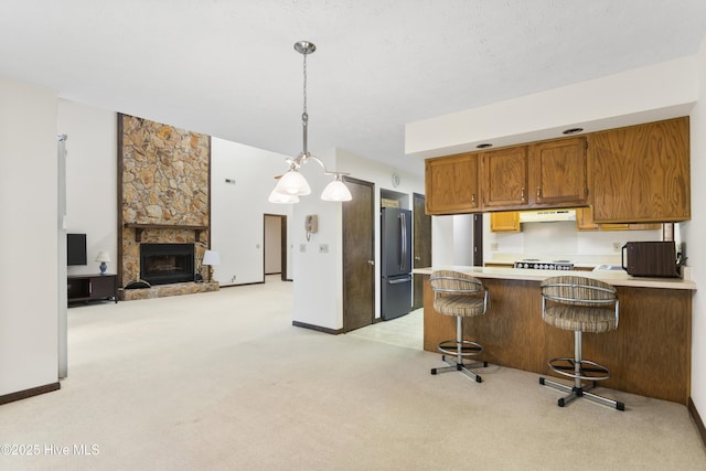 kitchen with light countertops, freestanding refrigerator, a peninsula, light carpet, and under cabinet range hood