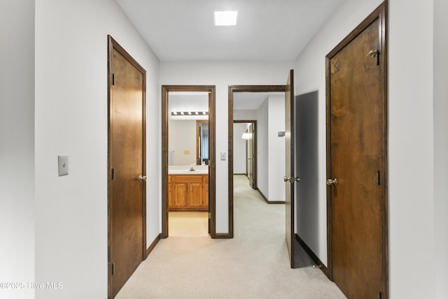 hallway featuring baseboards, a sink, and light carpet
