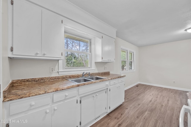kitchen featuring baseboards, light wood-style floors, stove, white cabinetry, and a sink