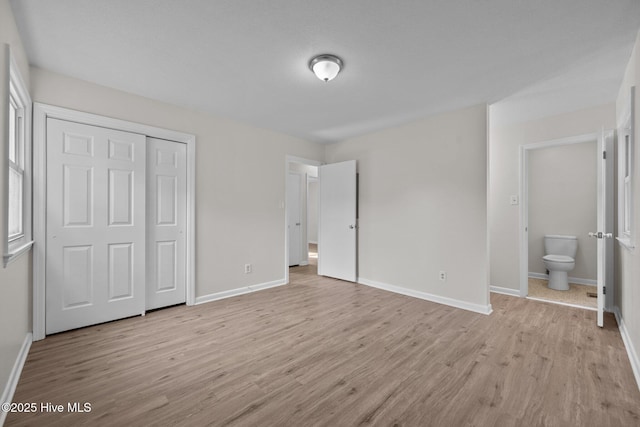 unfurnished bedroom featuring a closet, baseboards, light wood-style flooring, and ensuite bathroom