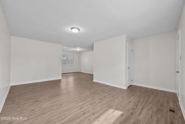 empty room with wood finished floors, visible vents, and baseboards