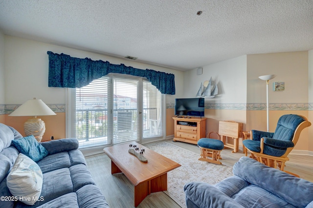 living area featuring visible vents, light wood-style flooring, a textured ceiling, and baseboards