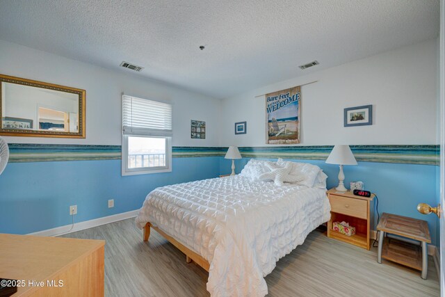 bedroom featuring visible vents, baseboards, a textured ceiling, and wood finished floors