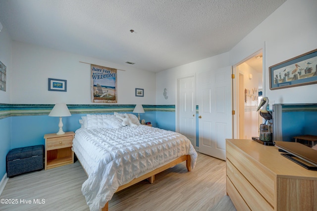 bedroom with light wood-type flooring, a textured ceiling, and visible vents