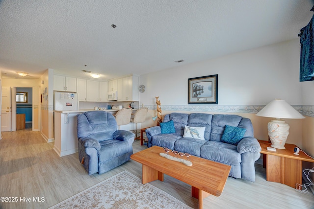 living area featuring visible vents, light wood-style floors, and a textured ceiling