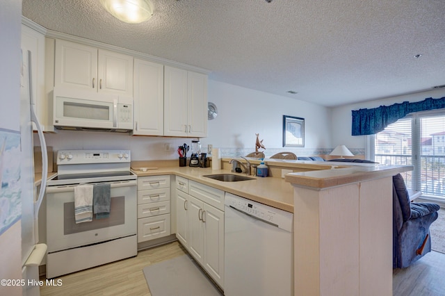 kitchen featuring white appliances, a peninsula, light wood-style flooring, a sink, and white cabinets