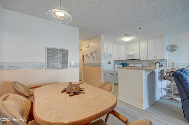 dining space featuring light wood-style floors, visible vents, and a textured ceiling