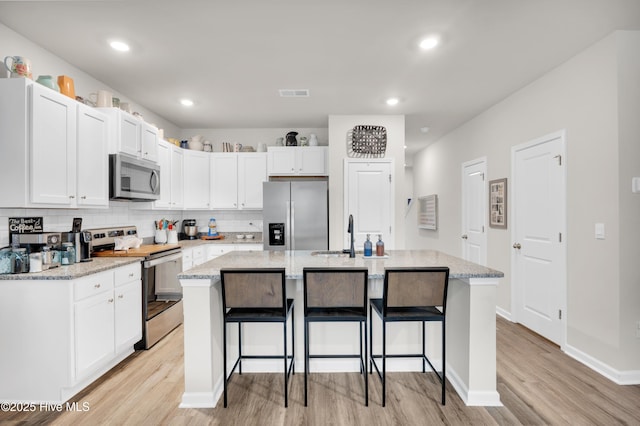 3659 Roseblossom Dr, Leland, NC 28451 - kitchen with a breakfast bar area, white cabinets, visible vents, and appliances with stainless steel finishes