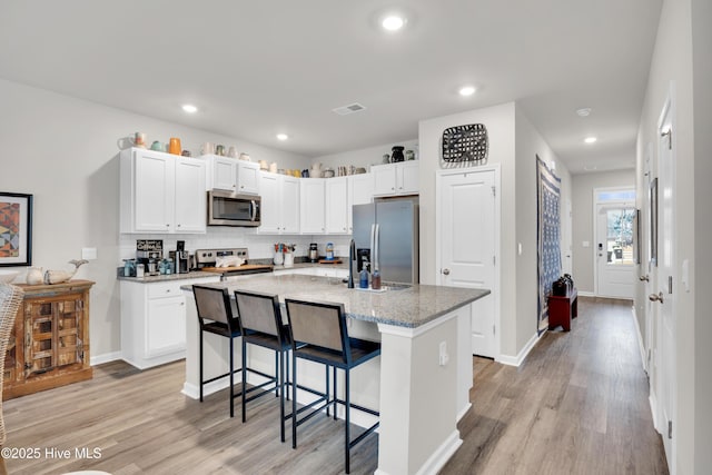 3659 Roseblossom Dr, Leland, NC 28451 - kitchen featuring visible vents, light stone counters, light wood-style flooring, a kitchen breakfast bar, and stainless steel appliances