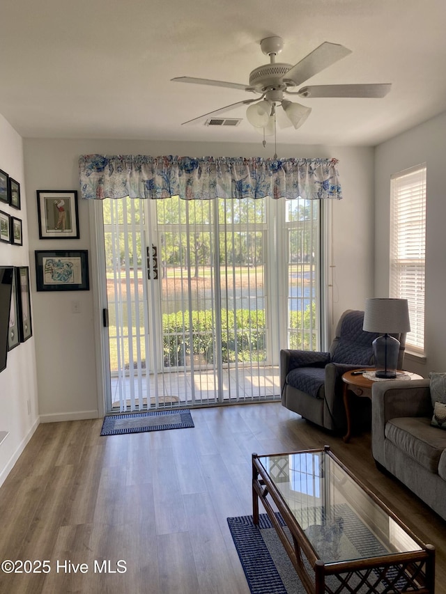 living room featuring baseboards, ceiling fan, visible vents, and wood finished floors